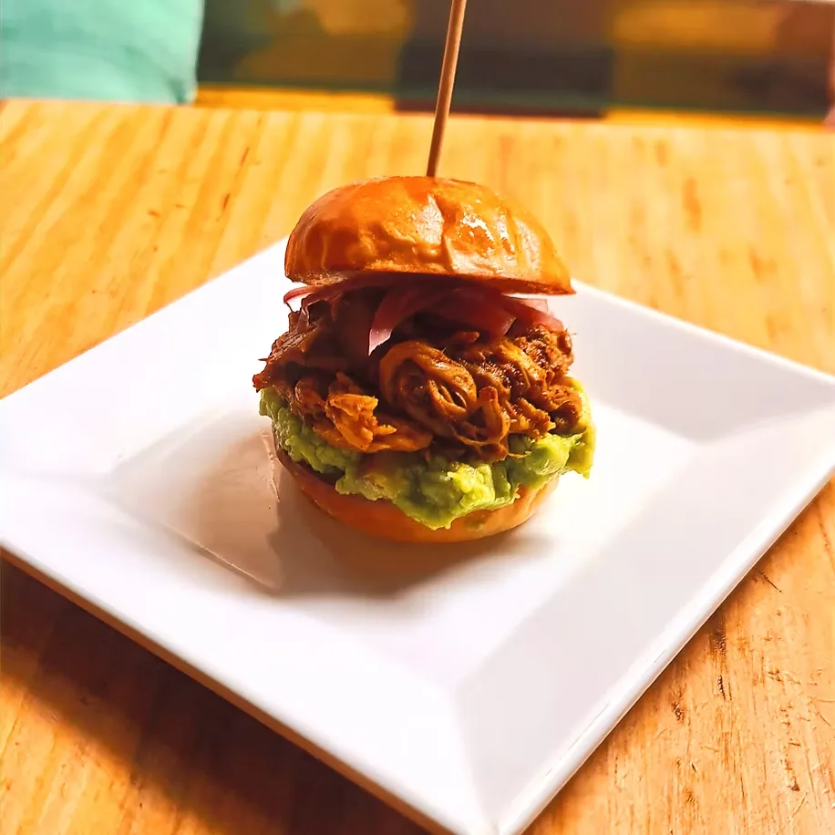 Mini burger de cochinita pibil con guacamole y cebolla encurtida, servida en plato blanco